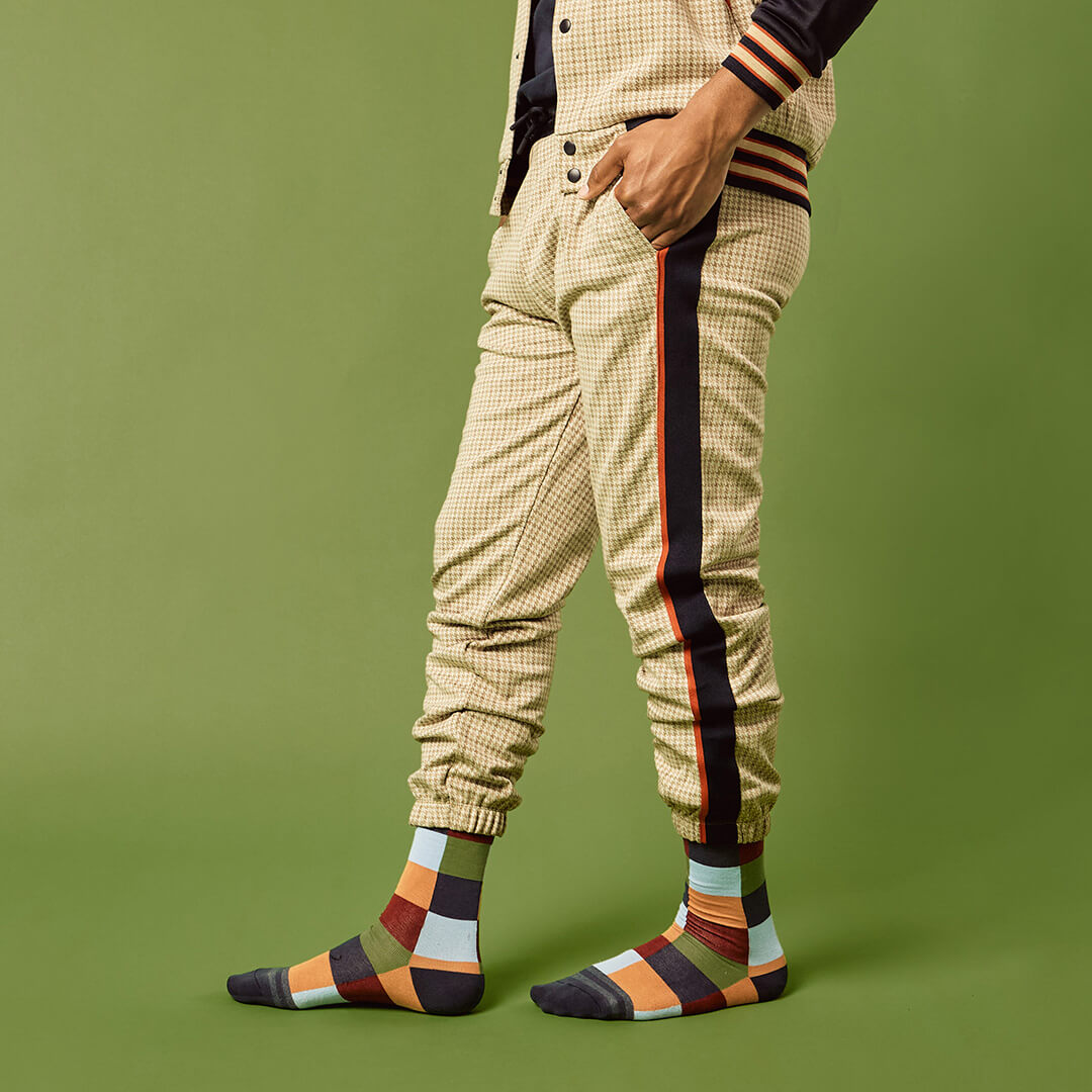 Person wearing checkered pants with side stripes and colorful socks on a green background