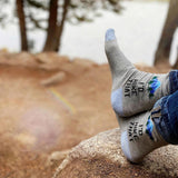 Person wearing socks with text and graphics, sitting on a rock outdoors. thumbnail
