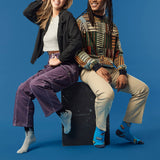 Two people sitting on a black box against a blue background wearing paint drip socks and cassette tape socks. thumbnail
