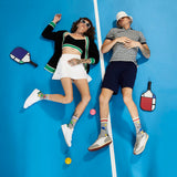 Two people lying on a blue surface with pickleball equipment around them.