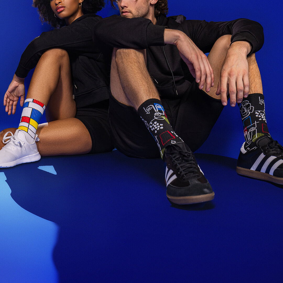 Two people sitting on a blue floor wearing colorful art-themed socks.