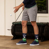 Person wearing socks with golf-themed designs, standing on a wooden deck with a golf club and ball.