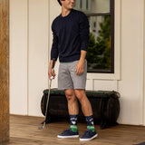 Man holding a golf club on a wooden deck with a neutral background