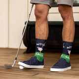 Person wearing socks with a golf theme and holding a golf club on a wooden floor.
