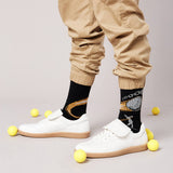 Person wearing black socks with graphic designs, beige pants, and white sneakers on a light gray background.