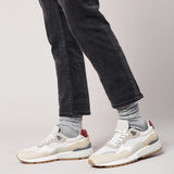 Person wearing white sneakers with red accents and gray jeans on a light gray background thumbnail