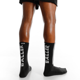 Black socks with 'BALLER' branding worn by a person on a white background