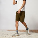 Person wearing olive green shorts and white sneakers on a neutral background
