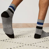 Gray socks with black toes and blue stripes worn by a person on a light wooden floor. thumbnail