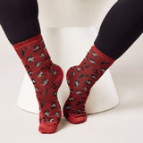 Red socks with black and white pattern worn by a person sitting on a white stool.
