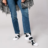 Person wearing blue jeans and cow print socks on a plain background thumbnail