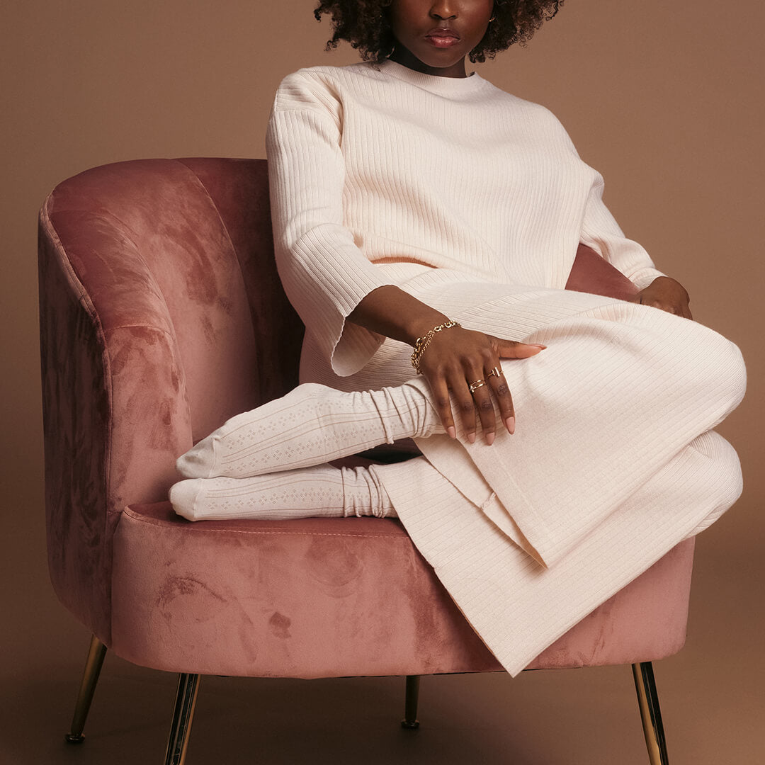 Person wearing a white outfit sitting on a pink chair against a brown background