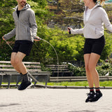 Two people jumping rope in a park with trees and benches in the background.