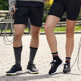 Two people wearing black athletic shoes and socks on a paved path.