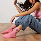 Woman wearing pink socks with the phrase "Women Unite," sitting on a wooden floor.