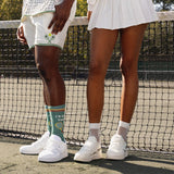 Two people standing on a tennis court and visible legs wearing tennis attire and crochet net socks.