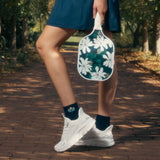Person holding a floral paddle and wearing pickleball socks in a park setting thumbnail